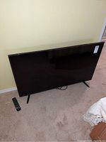 Front view of the Sharp 50 inch flat screen TV and remote on carpeted floor.