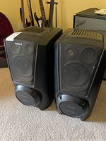 Pair of black Sony subwoofer speakers with front mesh grilles and S.A.W. branding, shown standing on carpet.