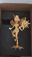Front view of the gold-plated Tinkerbell ornament resting in black foam inside the original box, showing detailed wings and star wand.