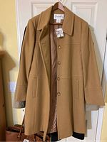 Camel wool Chadwick's overcoat hanging on wooden hanger against cream wall, showing front and buttons