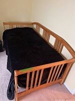 Full view of the wood trundle day bed with black quilted cover showing side and end rails with spindle design and curved top rails.