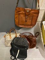 Overview of five handbags on grey surface, one hanging (Marco Polo) above four on table