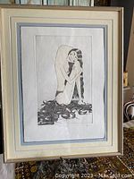 Framed black and white print featuring a nude figure with long hair wrapped around them, matted in double layers and behind glass.