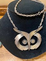 Front view of MCM owl pewter pendant on chain displayed on a black bust form, showing detailed owl face design with textured eyes and wings.
