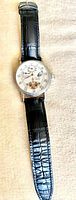 Full view of the Stauer automatic watch showing black leather band with crocodile pattern and white dial with open-heart design.