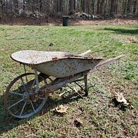 Side angled view of the antique wheelbarrow showing rust on metal basin and frame, with wooden handles extending behind.