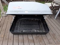 Open roof storage bin showing black interior base with some dirt and wear, hinged lid lifted.