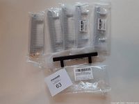 Six matte black cabinet handles/drawer pulls in original clear plastic packaging with barcodes and labels visible, laid out on a white surface.