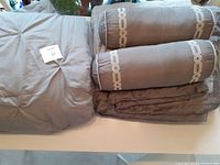 Set of two queen size comforters and two matching neck roll pillows displayed overlapping each other on a surface.