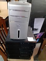Front view of Dell desktop tower on top with silver and grey casing, sitting on black Lenovo towers below