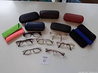 Overview photo of eight pairs of eye glasses arranged on table with six glasses cases and two cleaning cloths.