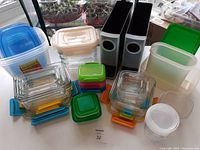 Overview of assorted glass and plastic food storage containers with colored lids and two black and silver Keurig pod holders.