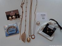 Full lot of jewelry including necklaces, earrings, bracelet, ring, and rose gold set in pouch on white background with lot number card