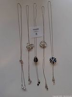 Five adjustable silver-tone necklaces laid flat on white background, showcasing their pendent designs and length-adjusting sliding stoppers.