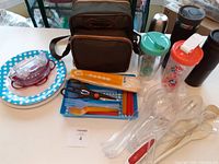 View of entire lot showing portable coffee maker bag, plastic plates, cutlery sets, tongs, and shakers