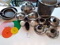 Wide view of all items on table showing pots, pans, lids, silicone lids, microwave egg cookers, shakers, and measuring cups
