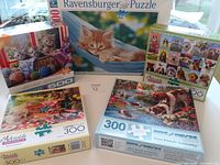 Five assorted cat and dog themed puzzles showing box covers, varying piece counts from 100 to 500 pieces, colorful photographic images, Ravensburger and Adorable Canines brands visible.