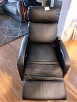 Black reclining chair shown fully reclined, showcasing cushioning, armrests, and footrest in extended position, with visible wear on upholstery.