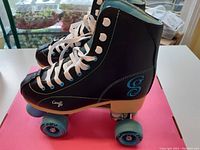 Side view of black roller skate boot with blue 'G' logo on heel and white laces tied up to the top eyelets.