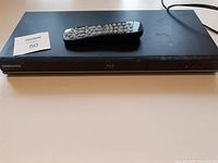 Front view of the Samsung Blu-ray Disc Player with remote placed on top, showing overall condition and layout.