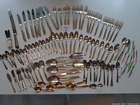 Full layout of all silverware items on white surface including knives, forks, spoons and novelty condiment knives.