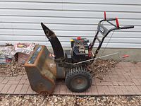 Side view of the snow blower showing rust on metal auger housing, large tires, and control handles.