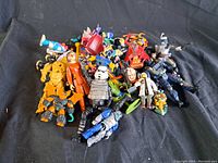 Pile of various action figures on a black cloth background showing a variety of characters and colors.