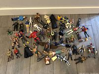 Photo showing around 35 assorted vintage action figures on floor, characters from Star Wars, Marvel, and other franchises