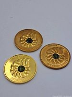 Three gold washed and bronze Korite coins with central green ammolite gemstone and sunburst pattern.