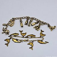 Two gold wash charm bracelets laid flat, one with marine animal charms and the other with assorted animal and figure charms.