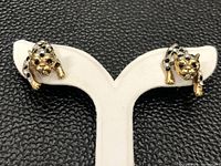 Front view of pair of gold-tone earrings shaped like leaping big cats with clear and black gemstones.