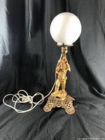 Front angle view of vintage cherub lamp on ornate pierced base with white frosted globe shade and power cord.