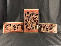 Overall view of the three Chinese wood carved pictures arranged together on a black background for scale and display