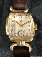 Front view of vintage Elgin Deco wristwatch showing square gold-tone case, white dial with Arabic numerals and sub-dial, and brown leather strap.
