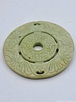 Top view of green circular carved stone pendant showing floral and textured central details.