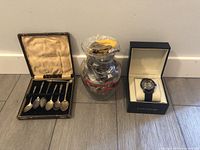 Full lot showing jewellery jar with lid, silver spoons in open case, and watch in box arranged on floor.