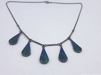 Full view of vintage necklace showing five teardrop pendants with blue and green stone inlays connected by bar links on chain.
