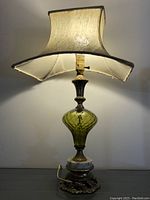 Full view of the lit lamp showing off the green glass body and fabric shade.