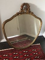 Front view of vintage shield-shaped mirror with ornate gold-tone frame featuring floral and bow design.