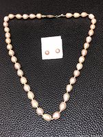 Full view of pearl necklace and pearl stud earrings on black textured surface.