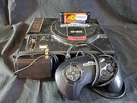 Sega Genesis console with controller, power adapter, and The Tick game cartridge inserted in cartridge slot.