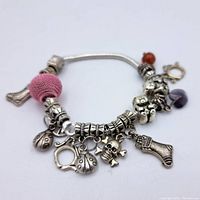 Photo showing the bracelet with multiple silver charms including pink bead, skull and crossbones, teddy bears, ladybugs, sock, heart, peace symbol, horseshoe, starfish, and orange bead.