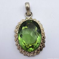Front view of oval green faceted stone set in scalloped sterling silver pendant.