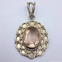 Front view of sterling silver pendant showing oval pink faceted stone and decorative frame.