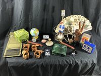 Full overview of the lot showing various vintage and decorative items including Asian fan, malachite ashtray, wooden napkin rings, lamp, piggy bank, peace sign hand sculpture, and other small collectibles.