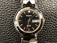 Close-up of Rado Jubile watch face showing black dial, silver hour markers, day-date window, and branding
