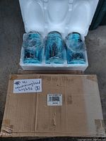 Front view of 3 hummingbird illuminated mason jar lights inside their foam packaging and still partially wrapped in plastic.