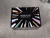 Black Morovan Professional Nail Art box on a concrete floor showing colorful design and branding.