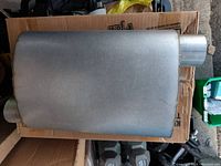 Top view of rectangular metallic muffler showing inlet and outlet pipes on opposite ends.