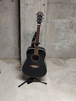 Front view of the black acoustic guitar on guitar stand against concrete wall